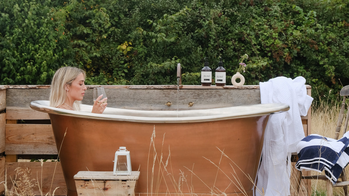 Woman relaxing in an outdoor bathtub with a view of greenery - courtesy of Kip Hideaways