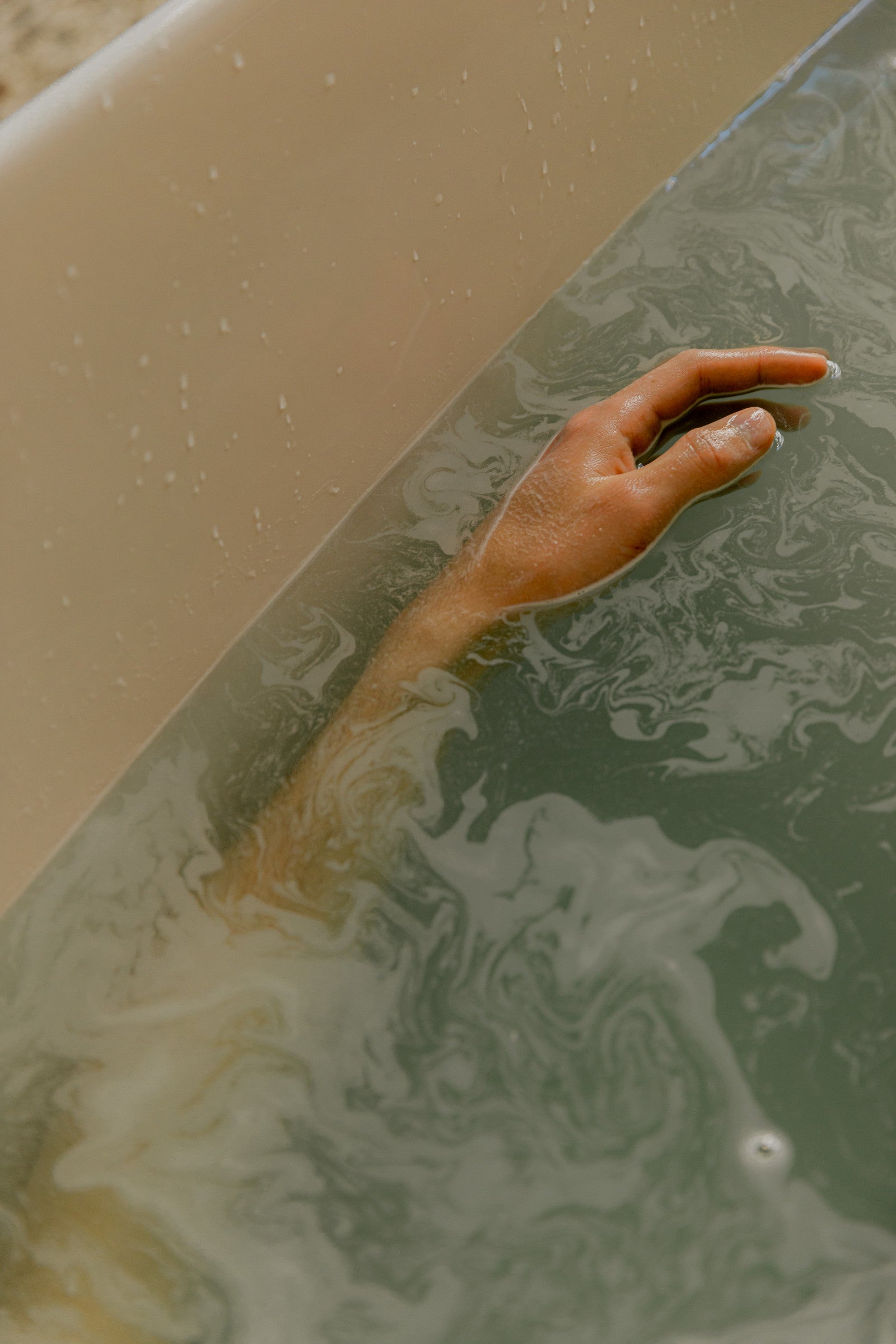 A hand trailing in sage green bath water