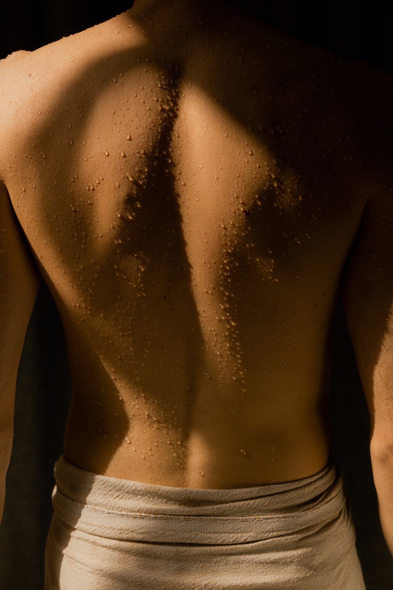 A bare back beaded with sweat after the sauna, a linen towel at the waist